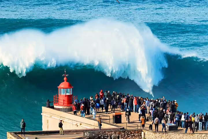 Tourists gather at the Nazaré lighthouse to witness the famous giant waves on a small group day tour from Lisbon to Fátima, Nazaré, and Óbidos.