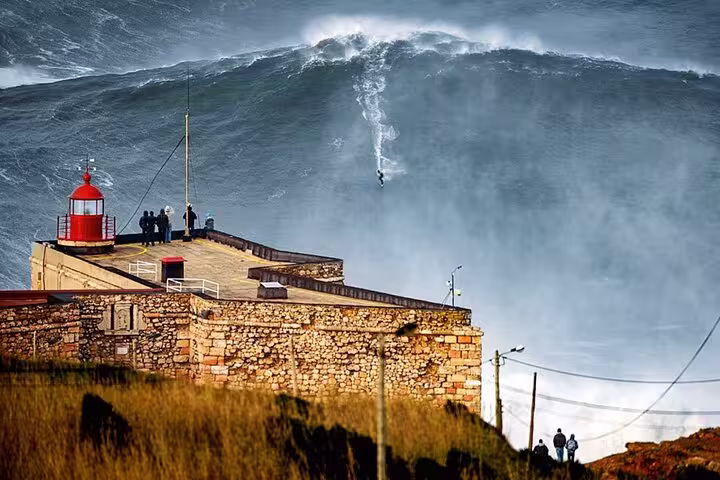 Massive wave crashes at Nazaré's iconic lighthouse, a highlight of the Fátima, Batalha, Nazaré & Óbidos private tour from Lisboa.