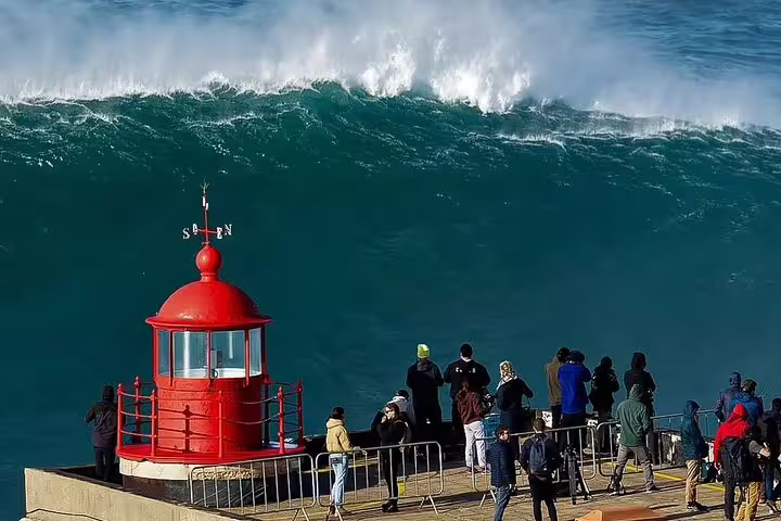 Tourists admire massive waves at Nazaré lighthouse, a highlight of the Fátima, Nazaré, and Óbidos full-day tour.