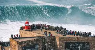 Crowd gathered at the lighthouse in Nazaré, Portugal, watching massive waves, a popular stop for customized Lisbon to Porto transfers.