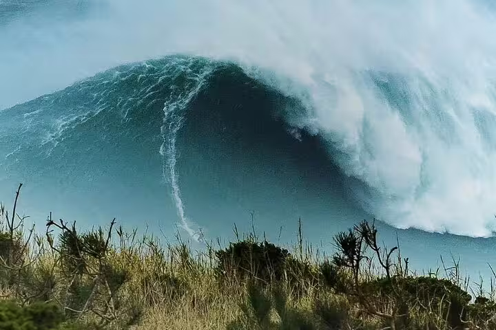 Massive ocean wave crashing along the coast of Nazaré, Portugal, showcasing the thrilling surf of this full-day tour.