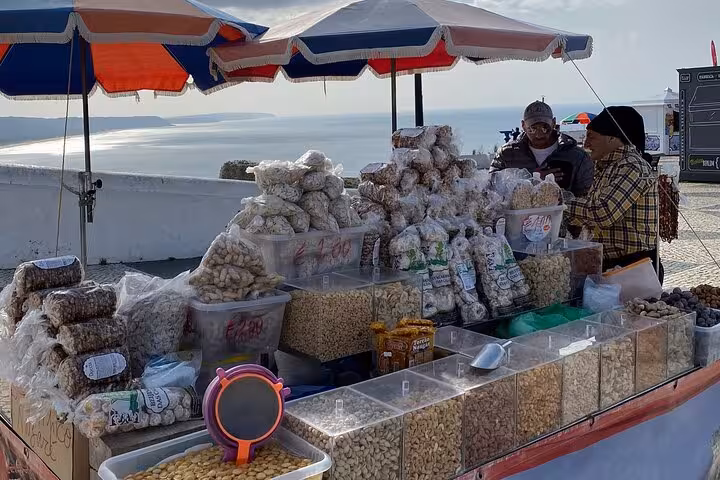 Traditional snack stall with nuts and local treats under colorful umbrellas in Nazare, Portugal, overlooking the sea.