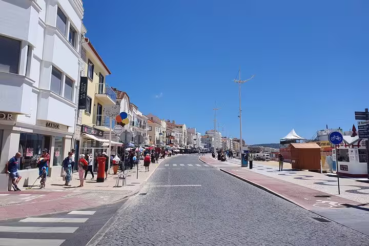 Scenic view of a bustling street in Nazaré, Portugal, showcasing vibrant buildings and tourists under a clear blue sky.