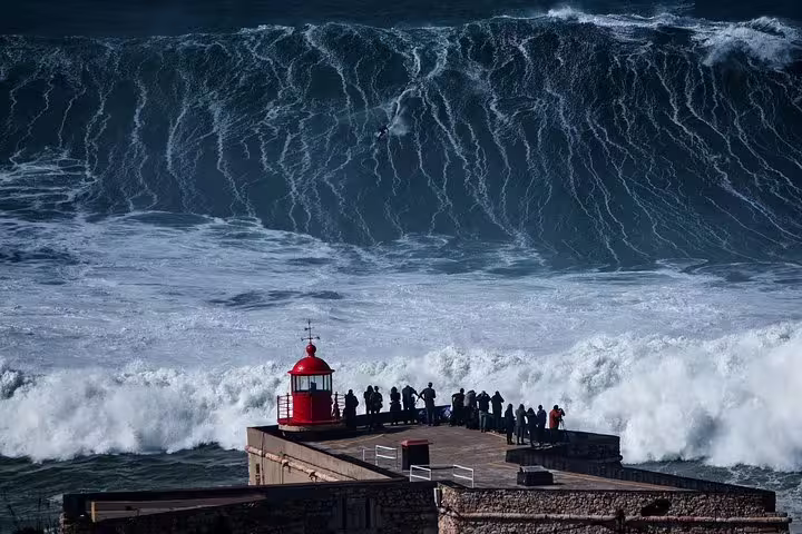 Tourists gather at the iconic red lighthouse in Nazaré, Portugal, to witness massive ocean waves during a full-day private tour.