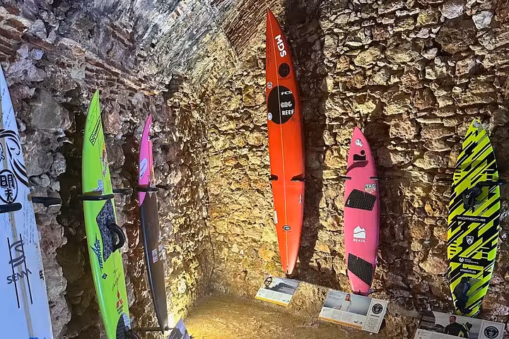 Colorful surfboards displayed against a rustic stone wall in Nazare, highlighting Portugal's surfing culture and adventure tourism.