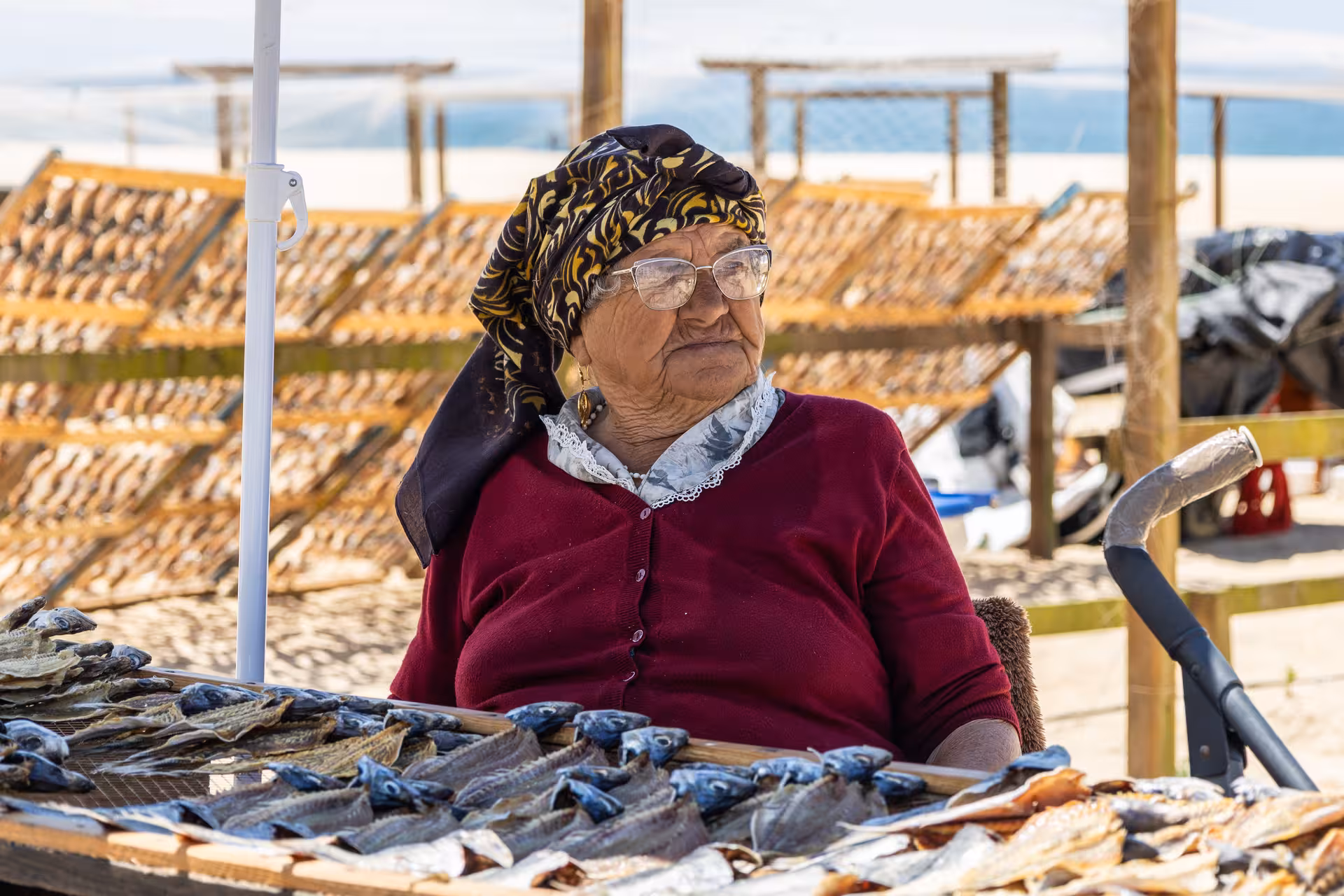 Local woman in traditional attire selling dried fish under the sun in Nazaré, Portugal.