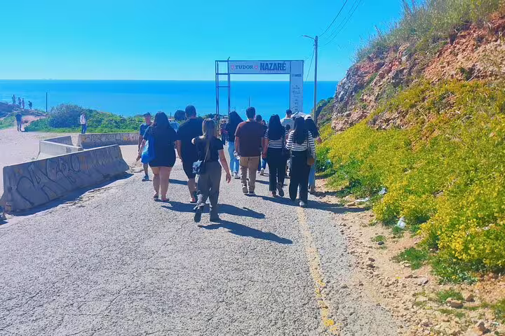 Tourists walking towards Nazaré’s iconic viewpoint, enjoying scenic coastal views and lush surroundings.
