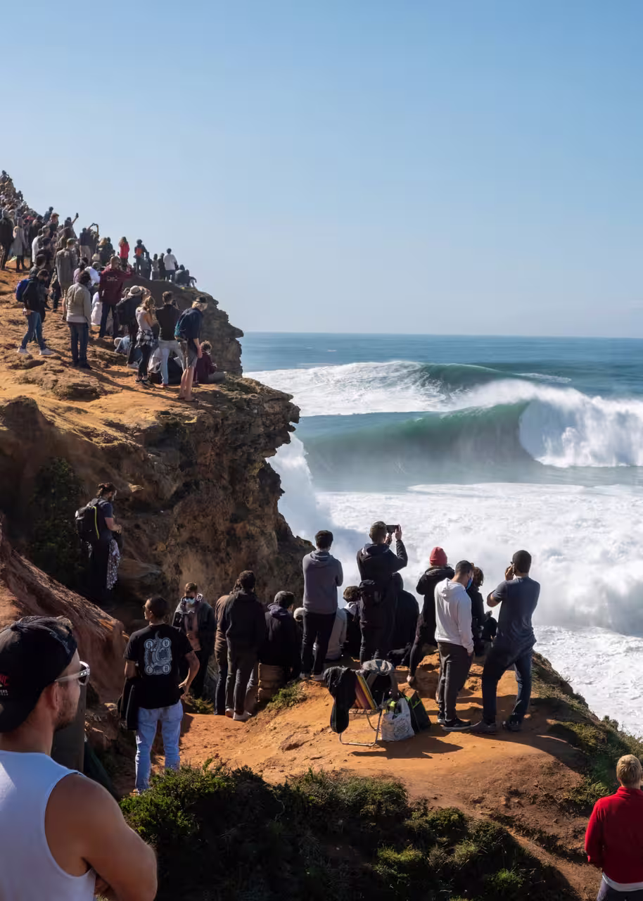Tourists admire the massive waves from a cliff in Nazaré, a popular stop on the Porto to Lisbon transfer route.