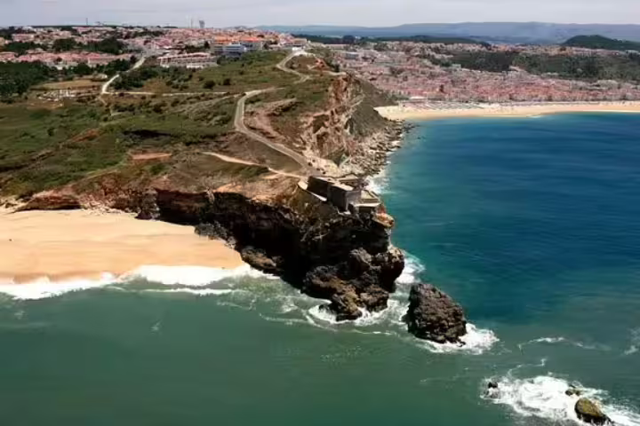 Aerial view of Nazaré's stunning coastline with golden cliffs and the Atlantic Ocean, part of a private Fatima and Óbidos tour.