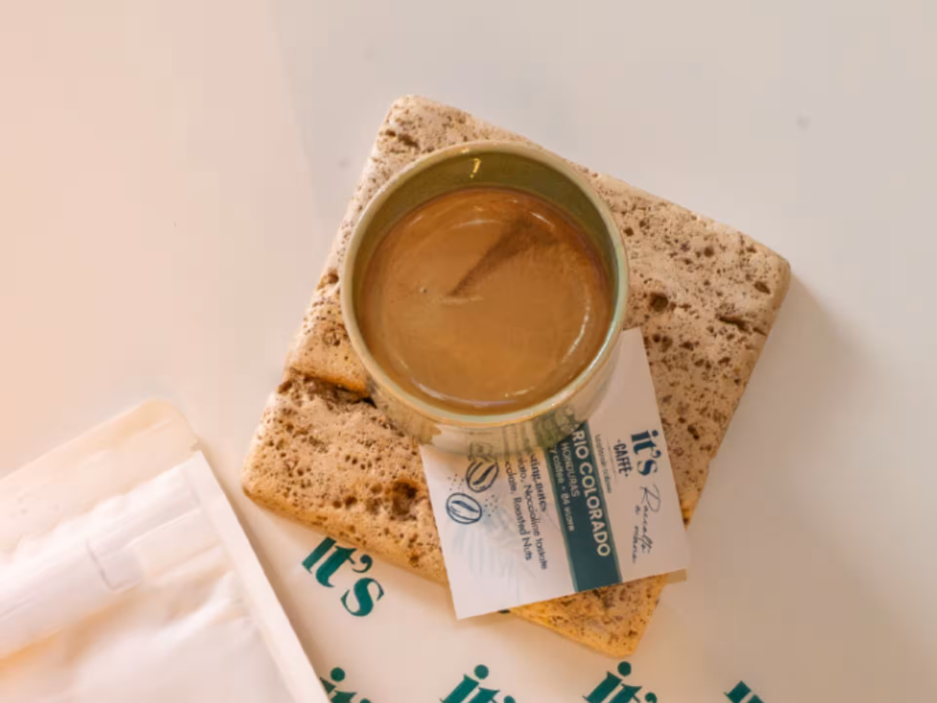 Rich Neapolitan espresso in a ceramic cup, placed on rustic stone coasters with branded packaging.