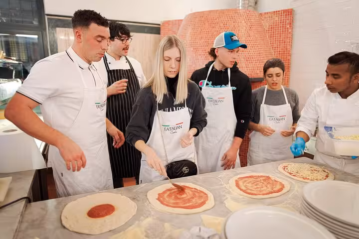 Attendees spread tomato sauce on pizza dough during a hands-on class in Rome's Piazza Navona area.