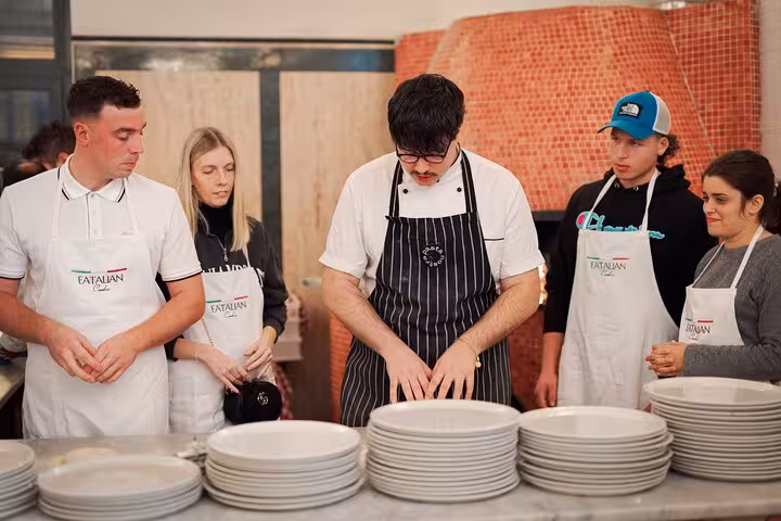 Chef demonstrates pizza preparation to attendees in a vibrant cooking class at Rome's Piazza Navona city center.