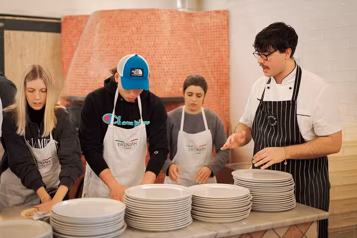 Instructor guiding students in a pizza cooking class with a traditional oven backdrop in Rome's Piazza Navona.