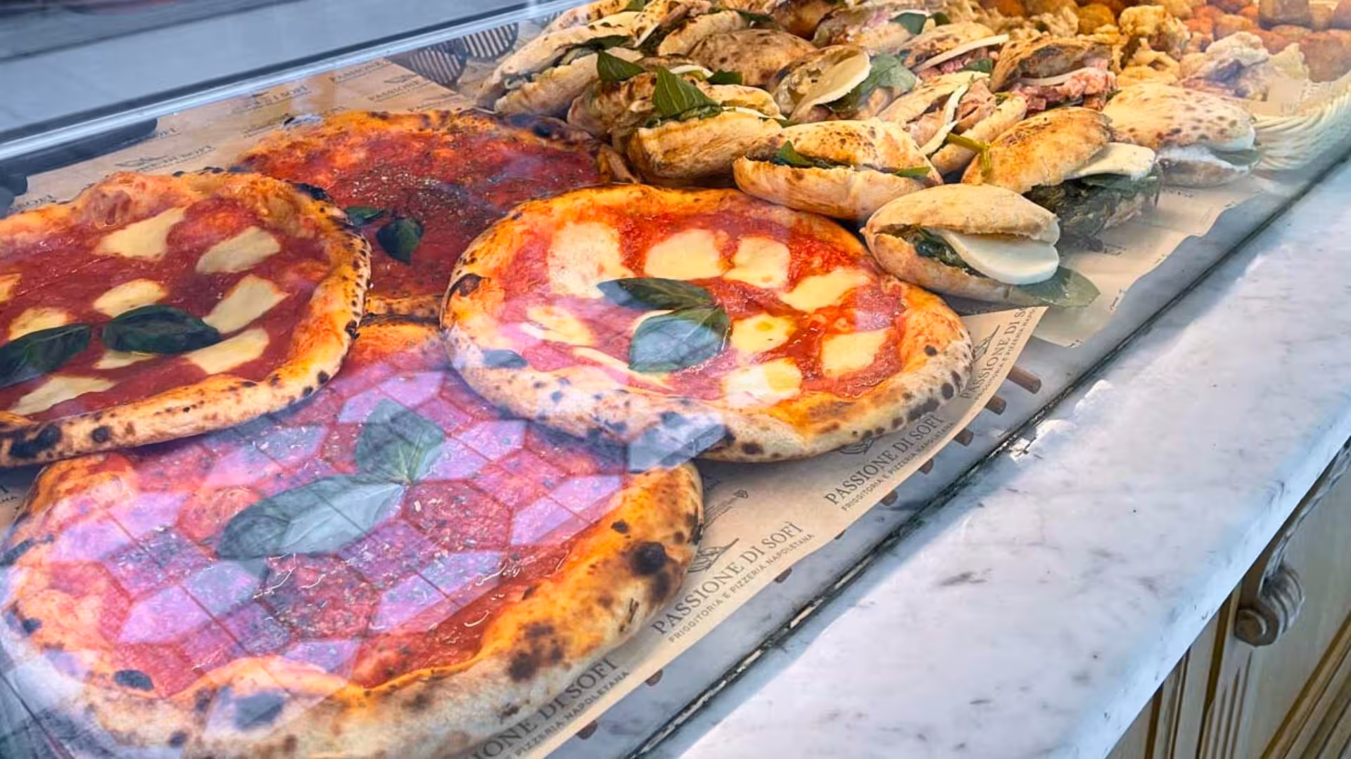 Selection of classic Neapolitan pizzas and panini in a display case on Spaccanapoli guided food tasting tour.
