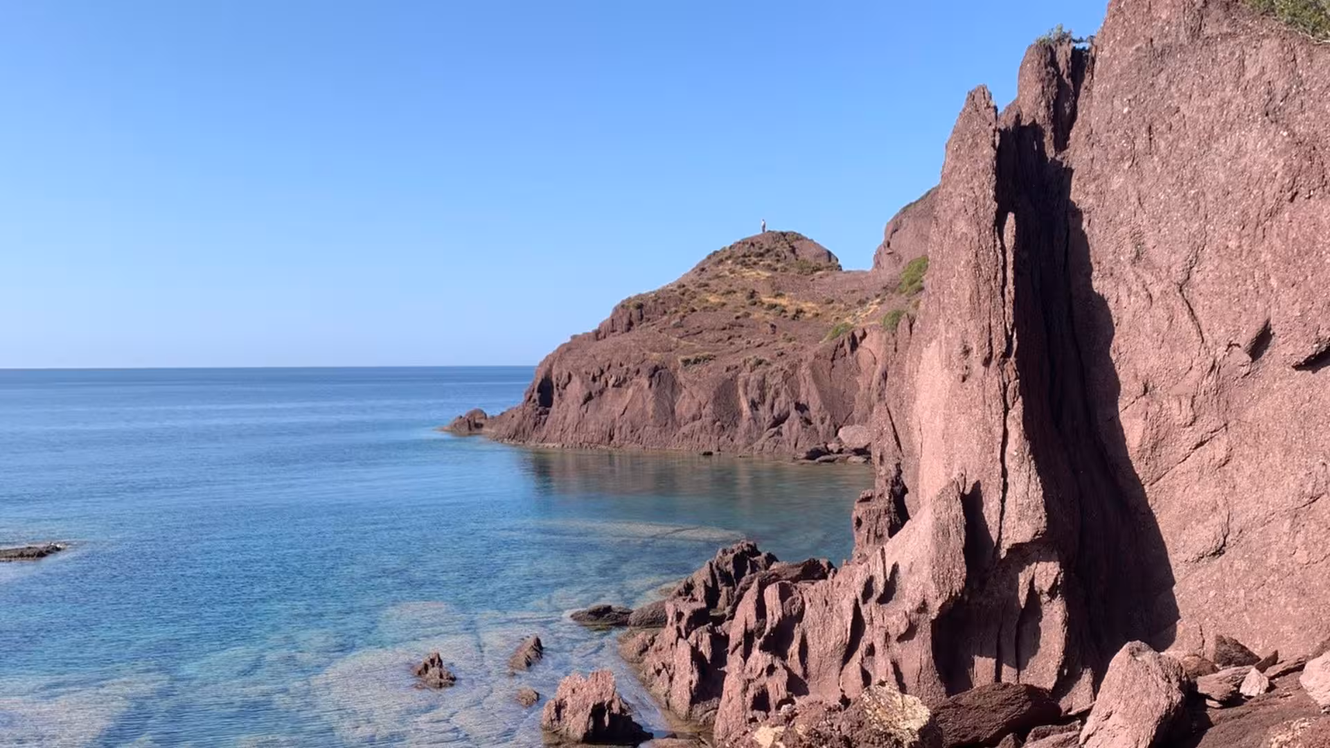 Stunning coastal view of red cliffs meeting clear blue waters on the Nebida to Masua hiking route.