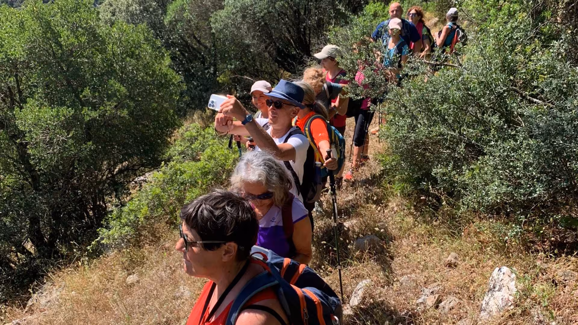 Hiking group capturing moments on a lush green trail from Nebida to Masua, surrounded by vibrant foliage.