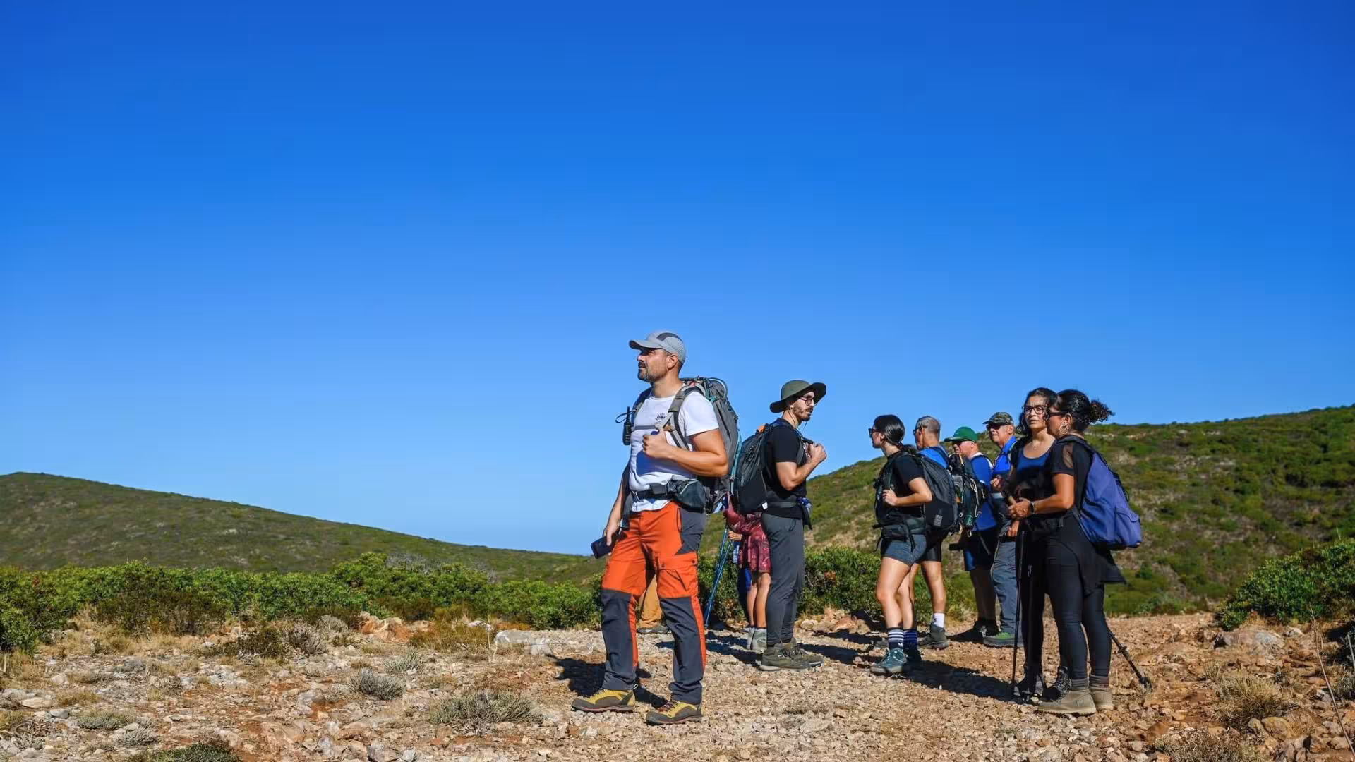 Group of hikers enjoying panoramic views on the trail from Nebida to Masua under a clear blue sky.
