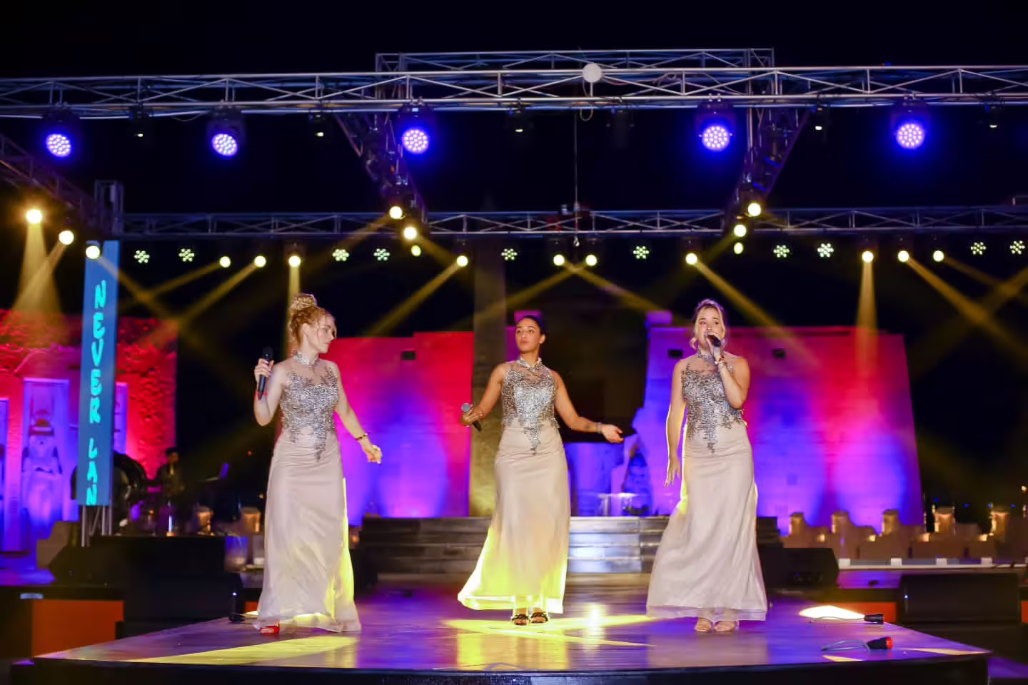 Trio of vocalists in silver gowns performing live at Neverland musical and cabaret show under spotlights