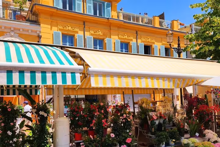 Colorful outdoor market in Nice features fresh flowers and striped awnings against charming architecture.