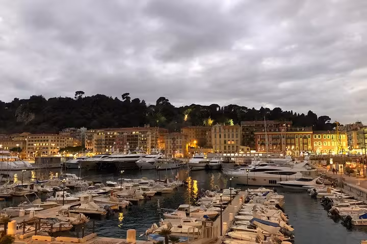 Scenic harbor in Nice at dusk with illuminated buildings, luxury yachts, and a serene maritime atmosphere.