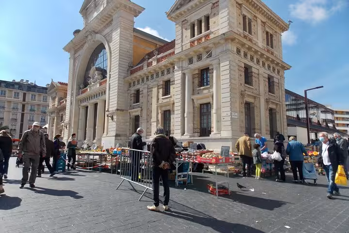 Bustling market scene in Nice with people exploring stalls against a backdrop of historic architecture.