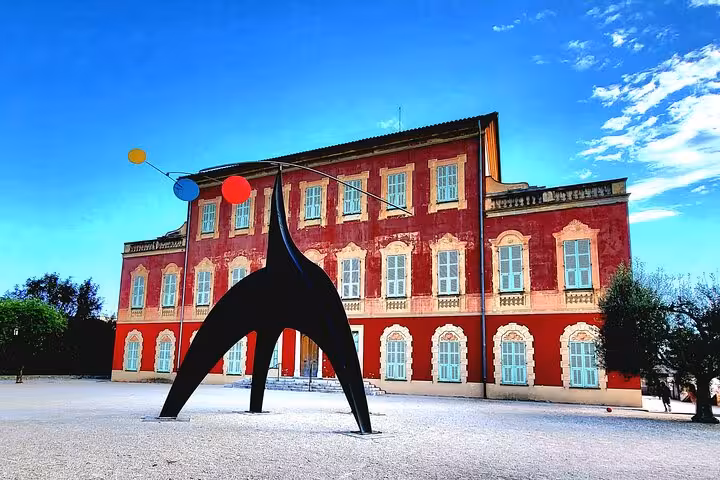 Striking modern sculpture in front of the historic Matisse Museum in Nice, under a clear sky.