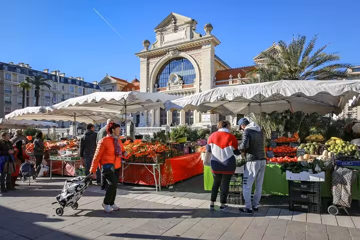 Outdoor market in Nice featuring vibrant produce and flowers under canopies with historic building in view.
