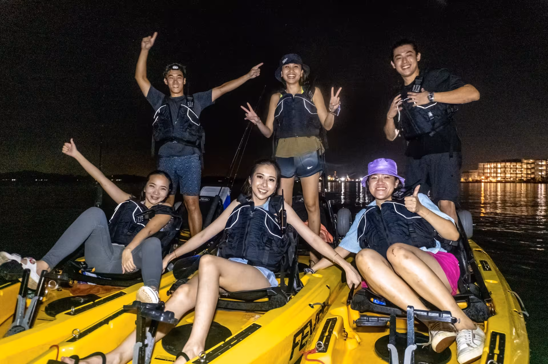 Group of friends in life jackets enjoying night kayak adventure at Pulau Ubin under a starlit sky.