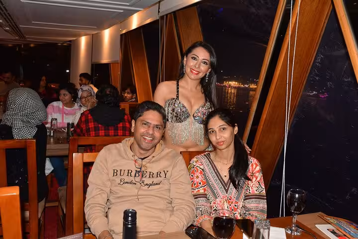 Guests enjoying a Nile cruise dinner with a smiling belly dancer adding to the vibrant atmosphere at night.