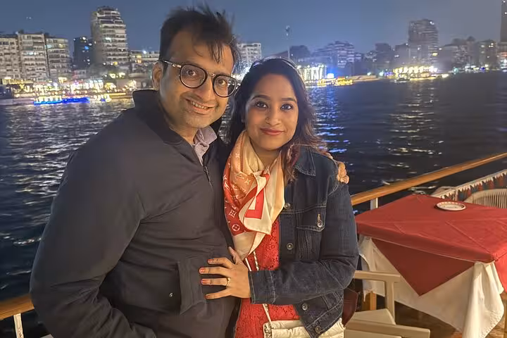 Couple smiling on a Nile cruise with city skyline and illuminated river in the background during a dinner tour.