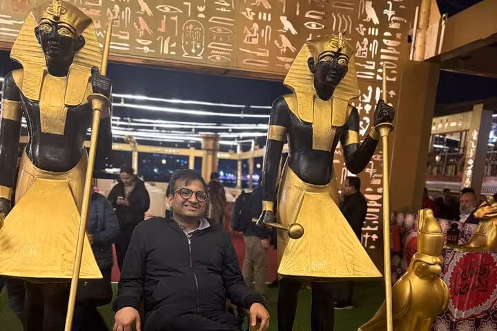 Tourist posing with Egyptian pharaoh statues on a Nile cruise with hieroglyphics and vibrant decorations.