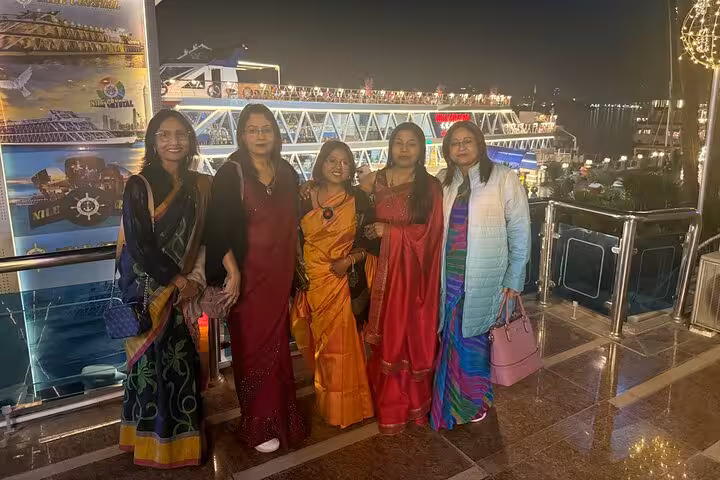 Group of women posing in vibrant attire by the Nile Cruise ship at night.