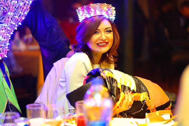 Guest enjoying Nile Maxim dinner cruise in Cairo with colorful Tannura show lights and festive onboard dining