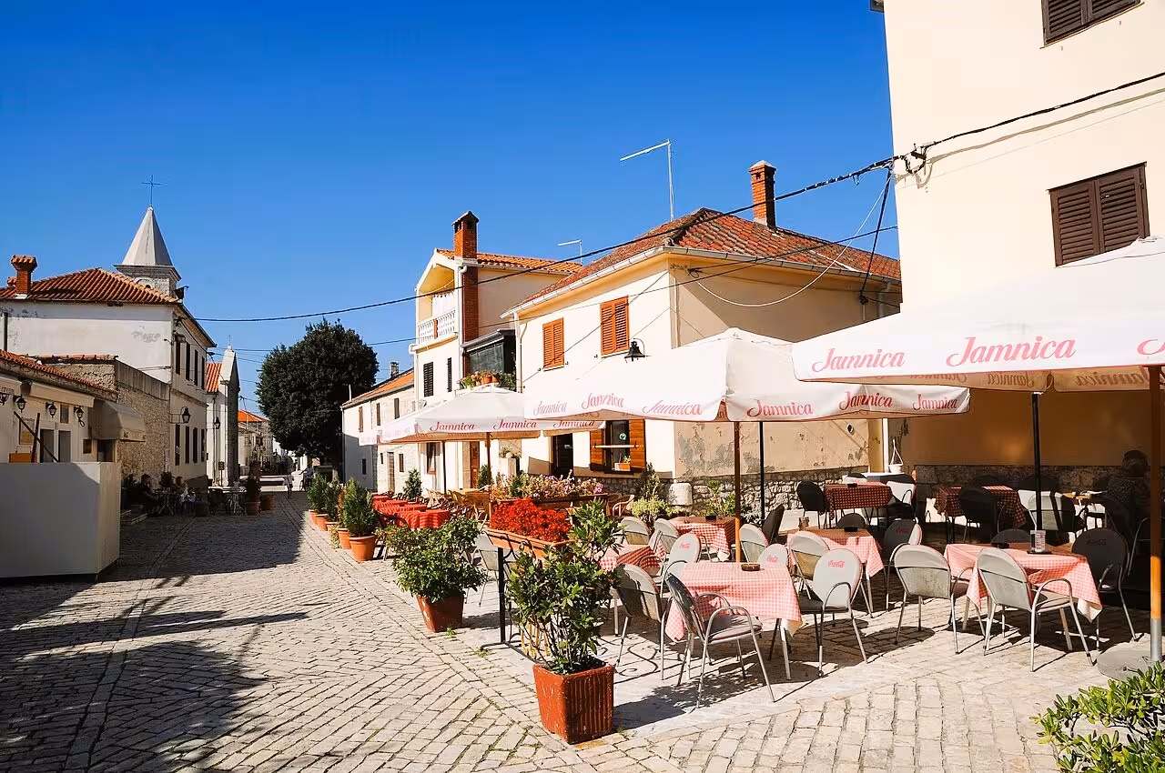 Sunny cobblestone street in Nin old town with café terraces, perfect stop on Nin & Zadar history tour