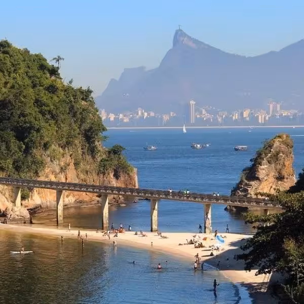 Stunning vista of Rio de Janeiro from Niterói beach, featuring a bridge and Christ the Redeemer in the background.