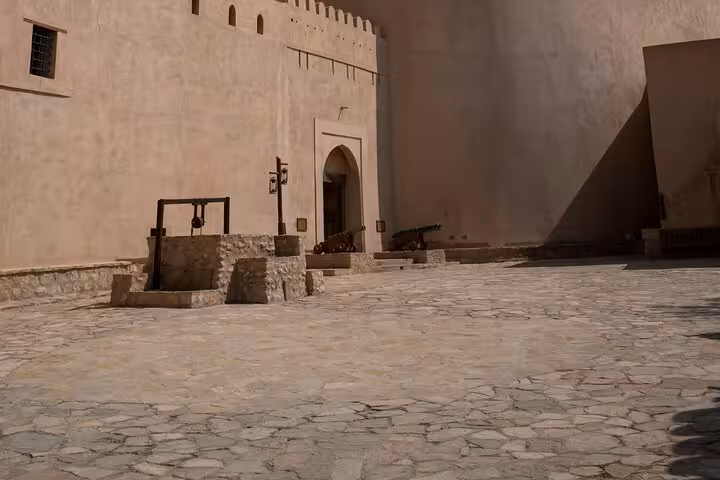 Historic courtyard of Nizwa Fort with stone well and cannons, a key stop on the Nizwa by Night sightseeing tour in Oman