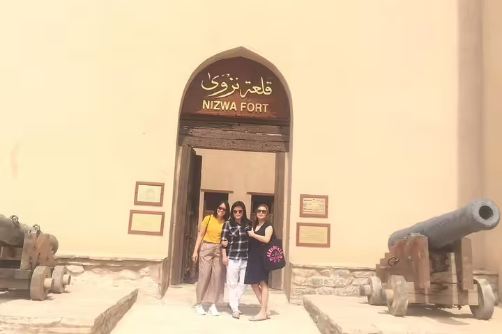 Visitors pose at the historic entrance of Nizwa Fort, a highlight of the Muscat full day private tour to Nizwa.