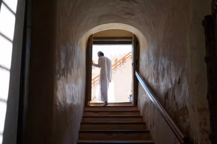 Visitor in white dishdasha walks up historic fort stairs in Nizwa, exploring heritage sites on an evening sightseeing tour