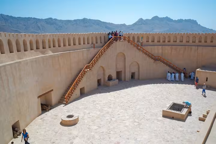 Visitors explore the sunlit courtyard and ramparts of historic Nizwa Fort on a private evening tour in Oman’s Hajar Mountains