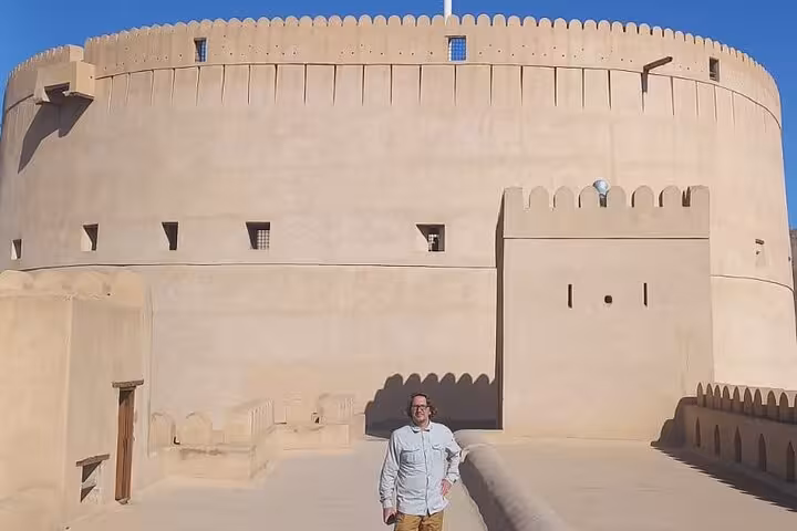 Tourist walking along sunlit walls of iconic Nizwa Fort, highlighting heritage architecture on a full-day Oman group tour