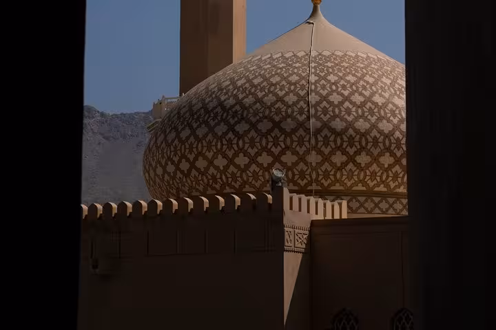 Ornate mosque dome and minaret beside Nizwa Fort walls at dusk, iconic skyline view on the Nizwa by Night sightseeing tour