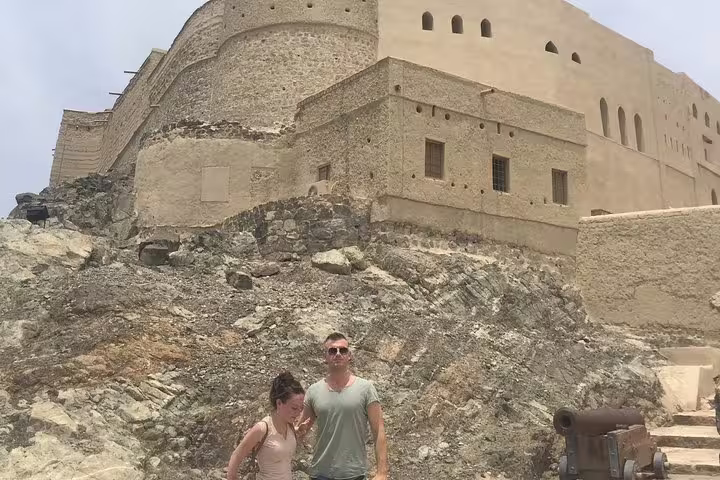 Visitors exploring the rugged exterior of Nizwa Fort, a highlight of the Muscat full-day private tour, showcasing its ancient charm.
