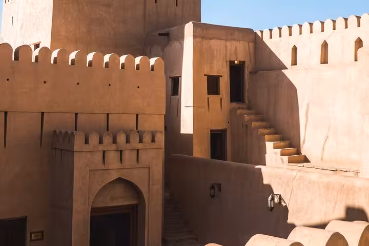 Sunlit mud-brick walls and stairways of historic Nizwa Fort, a key sightseeing stop on private transfer from Muscat