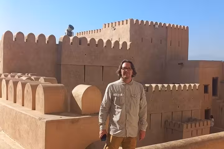 Traveler standing on the ramparts of historic Nizwa Fort in Oman, enjoying panoramic views on a full-day guided tour