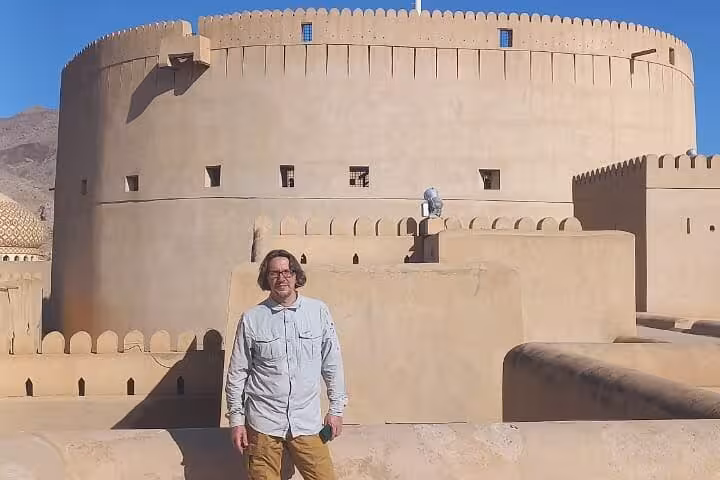 Visitor standing on the ramparts of historic Nizwa Fort, enjoying panoramic views during a full-day Oman group tour