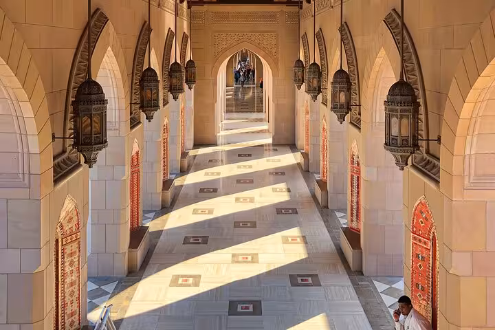 Golden evening light fills an ornate mosque corridor in Nizwa, Oman, highlighting arches, lanterns and intricate Islamic design.