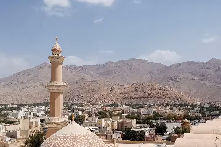 Panoramic view of Nizwa mosque minaret and old town framed by Hajar Mountains on a full-day group tour in Oman