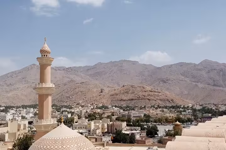 Scenic view of Nizwa mosque minaret and old town at sunset with dramatic Hajar Mountains backdrop on private evening tour