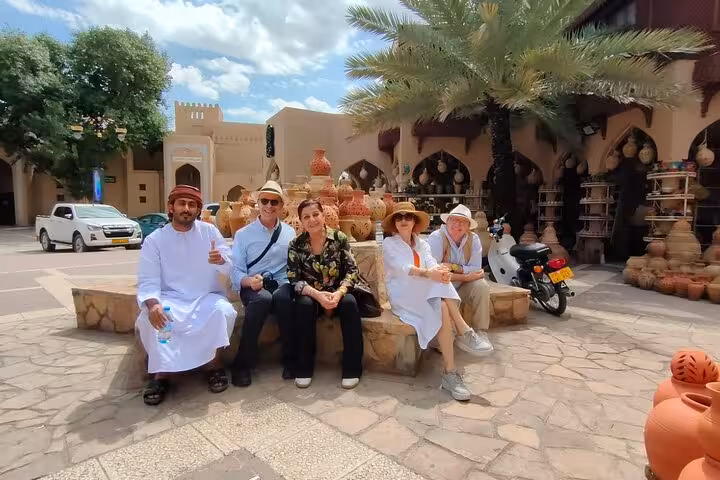 Tourists relax by traditional pottery stalls at Nizwa souq, enjoying a cultural stop on the Nizwa by Night sightseeing tour in Oman