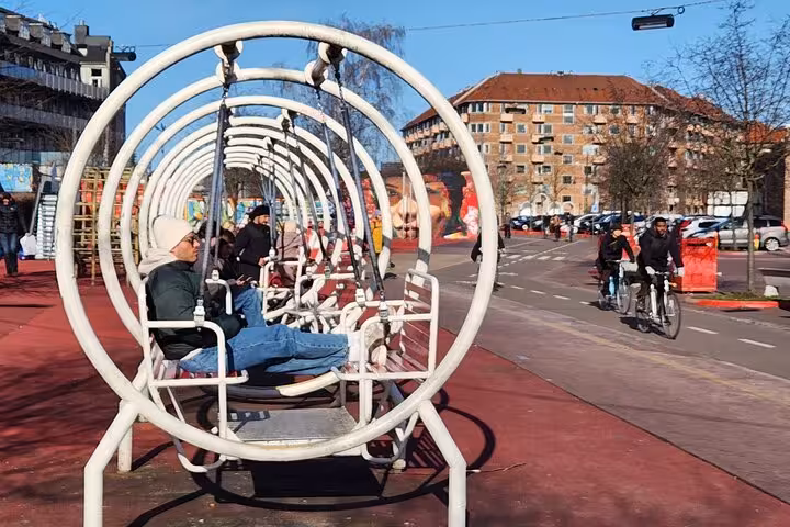 Visitors relaxing on unique swing benches in a lively public space in Copenhagen, showcasing Danish urban life.